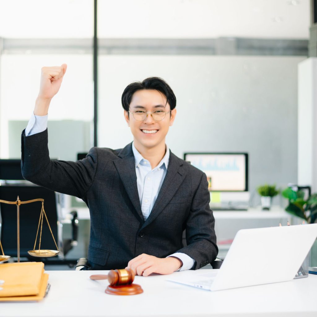 Confident Asian lawyer using tablet with gavel and justice scales on desk, looking at camera. Perfect for law, justice, business, and modern legal technology themes.